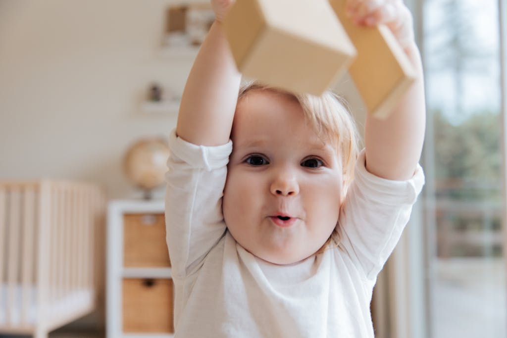 Entzückendes Baby, das in gemütlicher Innenumgebung mit Holzklötzen spielt. Es freut sich über die Förderung durch Berlinpass BuT