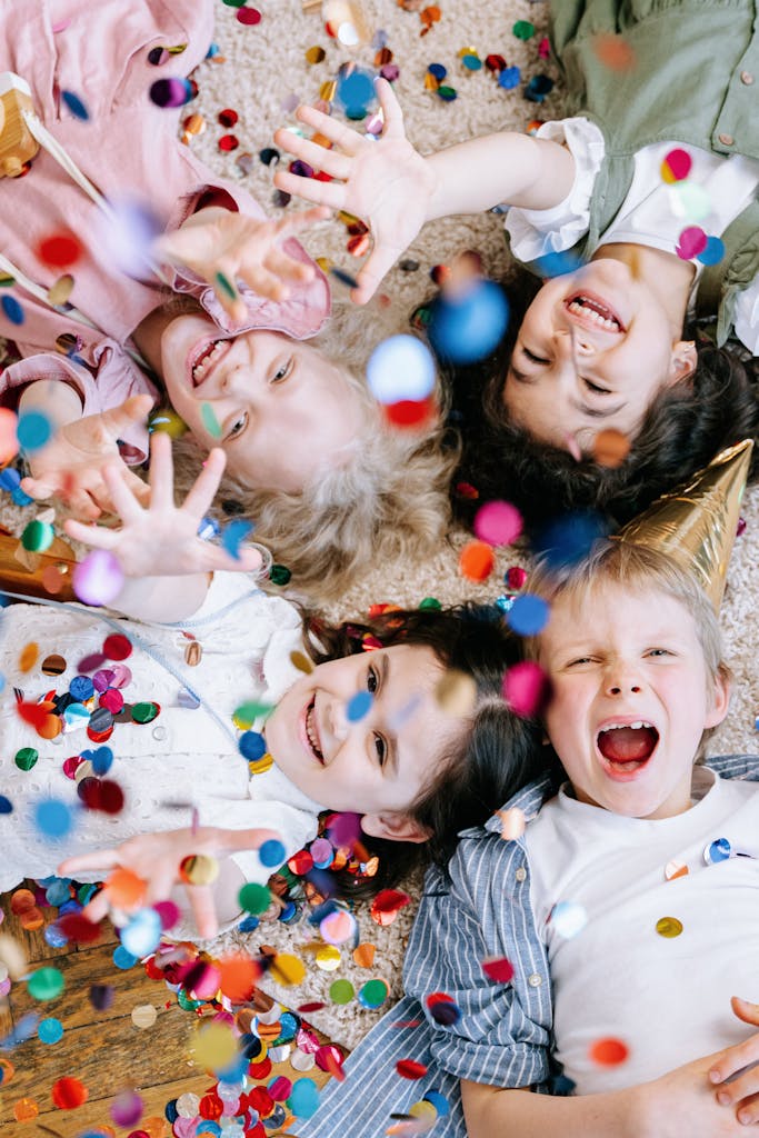 Vier fröhliche Kinder liegen auf dem Boden, spielerisch umgeben von buntem Konfetti. Sie feuen sich über die Förderung durch Berlinpass BuT.